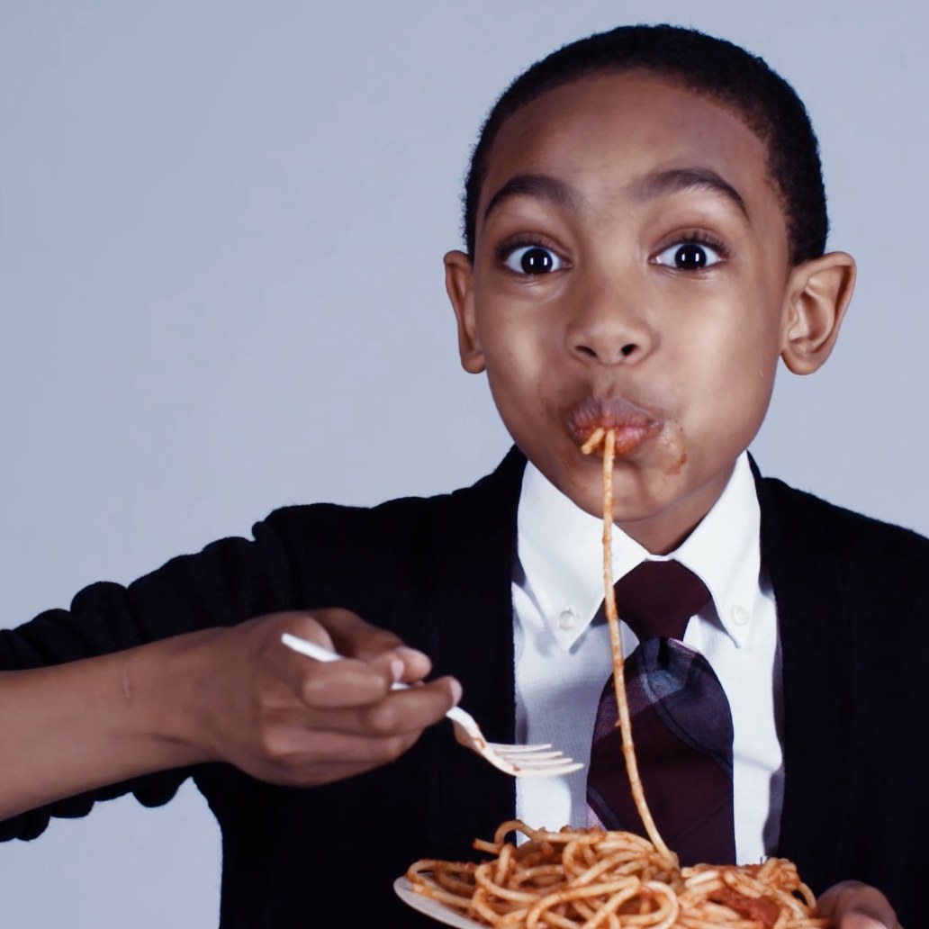 A boy in a suit eating spaghetti